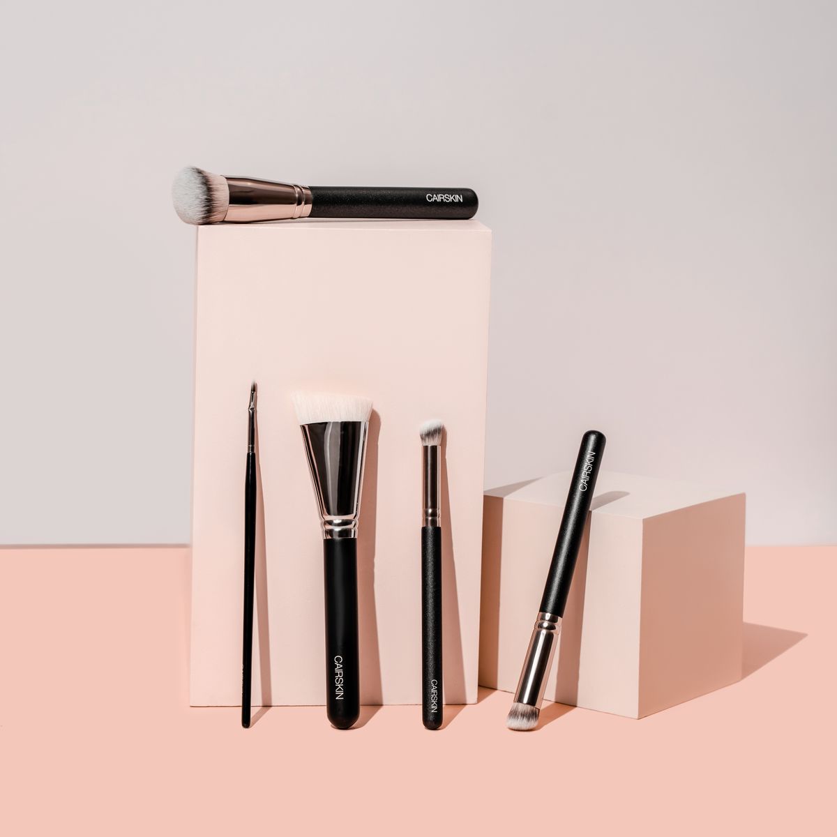 Black CAIRSKIN makeup brushes standing against blush-coloured blocks