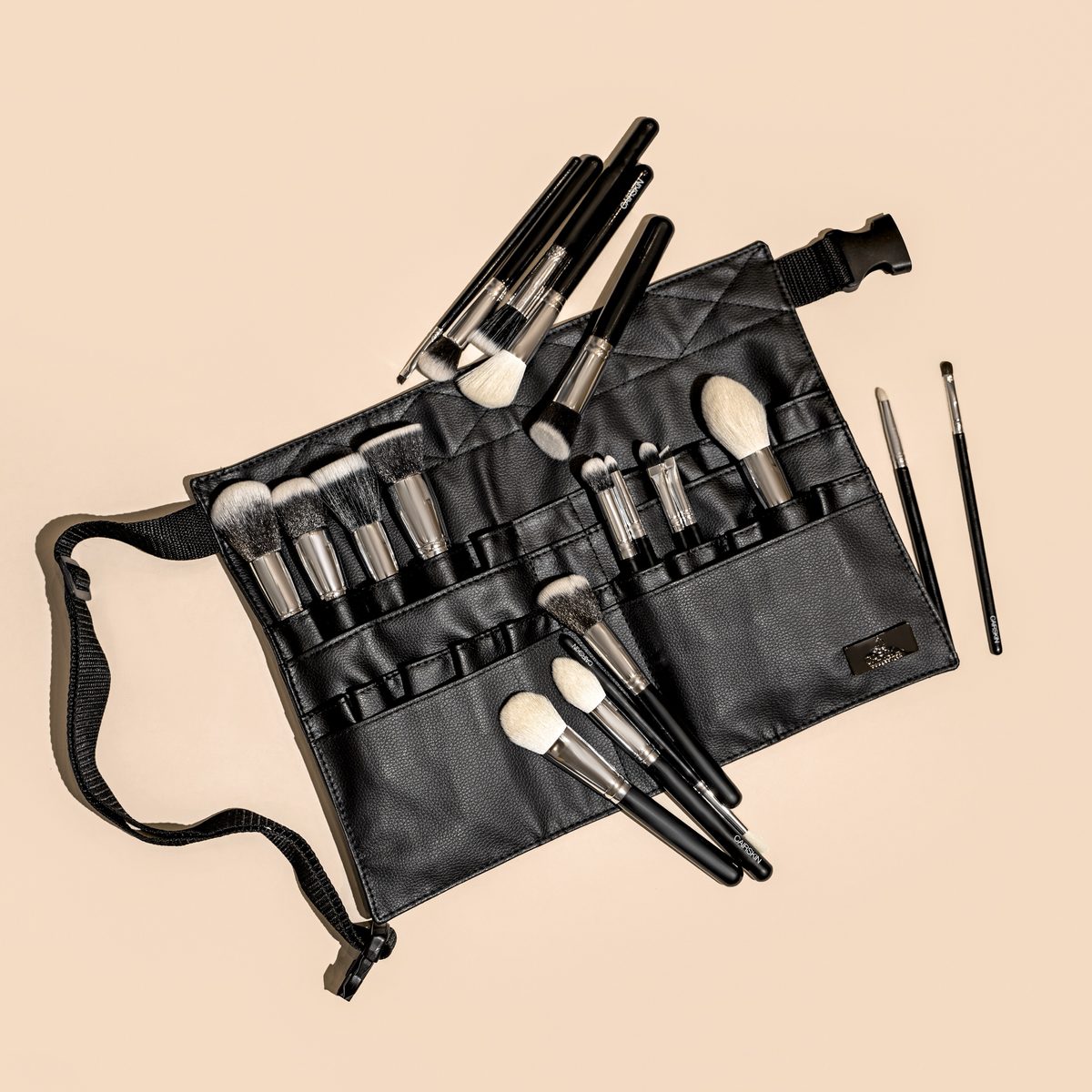 Black CAIRSKIN brushes in a professional brush belt on a warm beige background